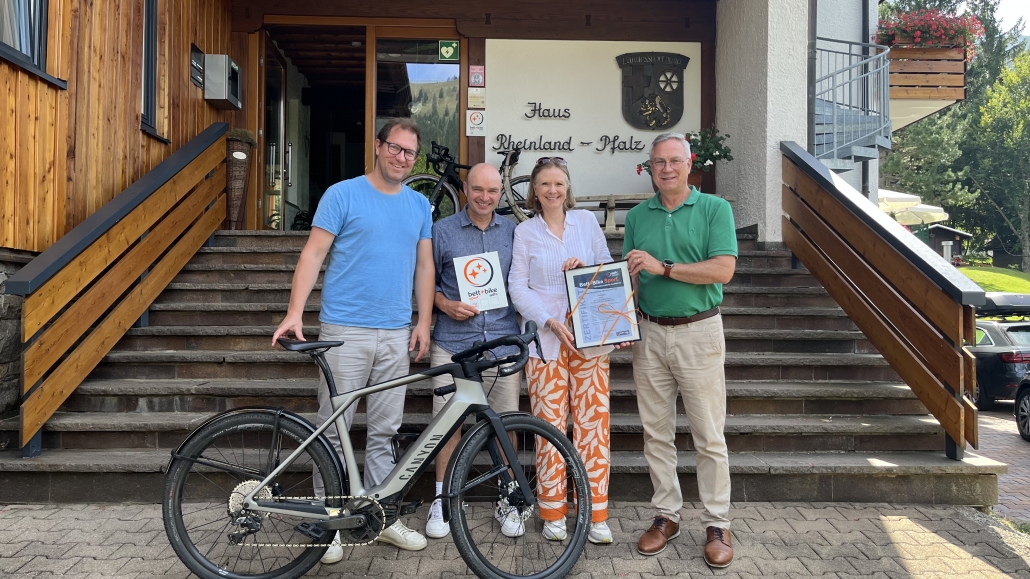 Vier Personen stehen nebeneinander, zwei halten eine Urkunde in den Händen, vor ihnen steht ein Fahrrad.